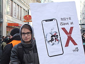Ein Südwind-Aktivist hält vor einem Apple-Store ein den Konzern kritisierendes Schild hoch