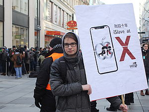 Ein Südwind-Aktivist hält vor einem Apple-Store ein den Konzern kritisierendes Schild hoch