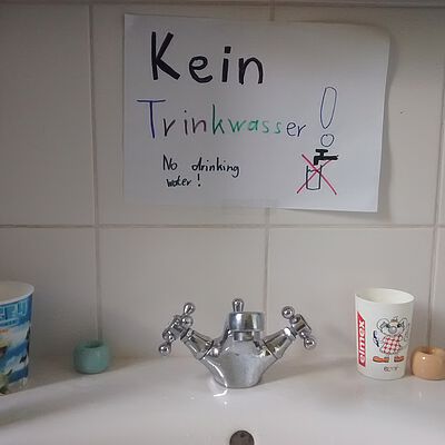 Wasserhahn und Waschbecken. Dahinter befestigt ein Zettel mit dem Text "Kein Trinkwasser!"