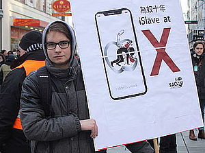 Ein Südwind Aktivist macht mit einem Schild auf die miserablen Arbeitsbedingungen beim Konzern Apple aufmerksam