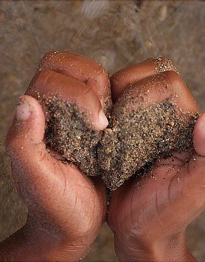 Zwei Hände formen ein Herz und halten dabei Sand. Im Hintergrund Meer und Sand